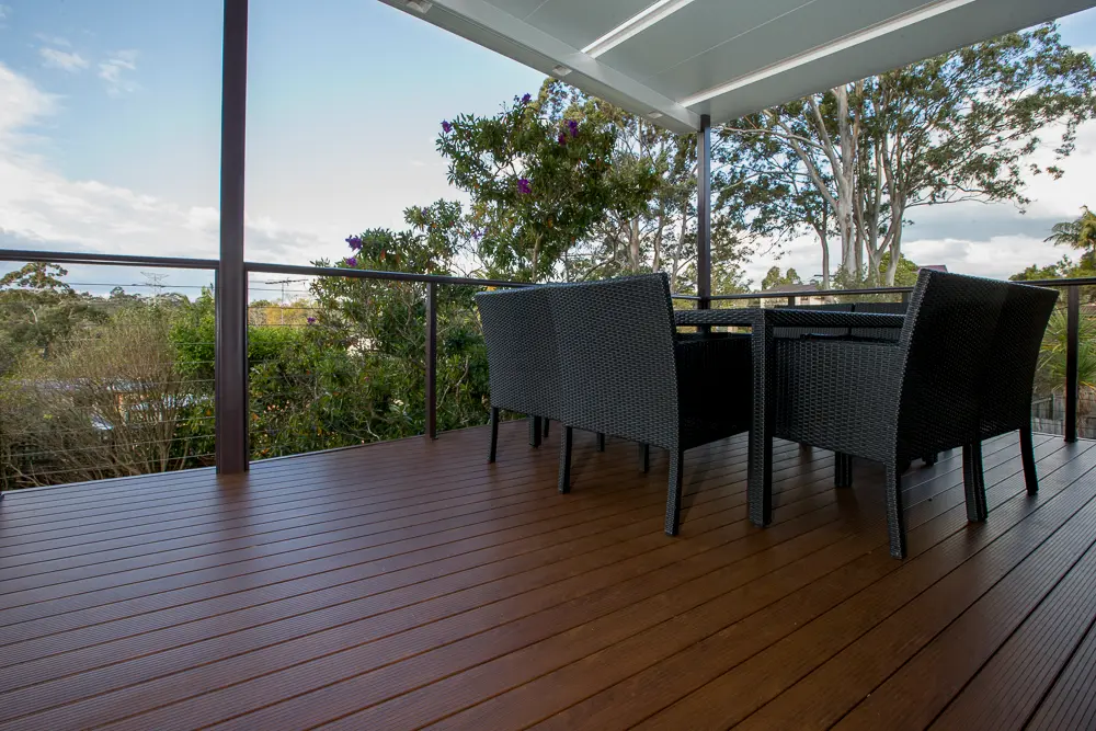 A modern elevated deck with a glass balustrade and outdoor seating, surrounded by lush trees, providing a peaceful and private retreat.