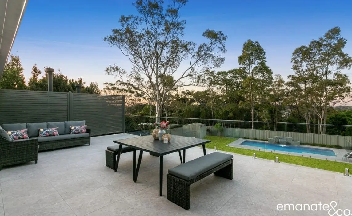 A contemporary tiled outdoor dining patio with a black table, bench seating, and a view of the backyard pool, ideal for outdoor entertainment.