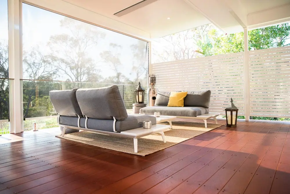 A contemporary outdoor living space with a timber deck, plush seating, and privacy screens, creating a cozy and elegant entertainment area.