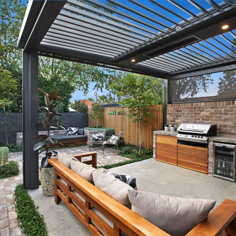 Custom opening louvred roof patio pavilion and brick outdoor kitchen in Cammeray, featuring an integrated flush ceiling heater, downlights, concrete floor, and premium timber lounge seating.