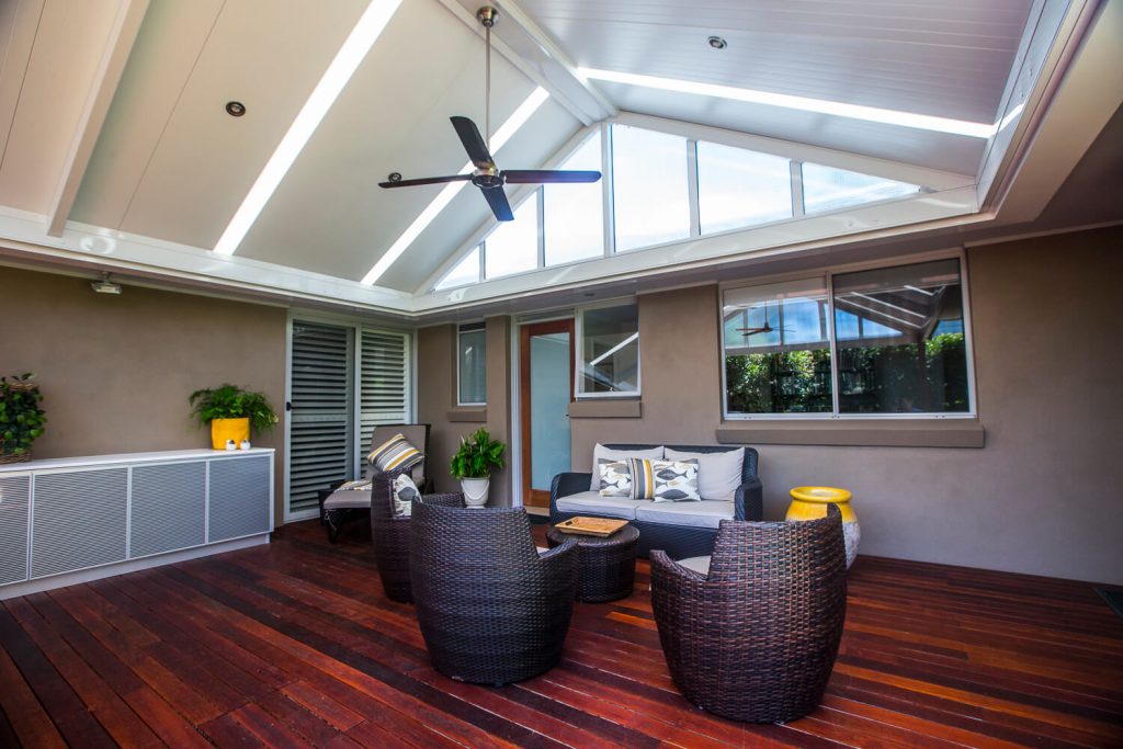 Custom architectural gable patio roof extension in Hornsby, featuring integrated translucent skylight strips, a high white insulated ceiling with a fan, a glass infill wall, and a luxury hardwood timber deck lounge.
