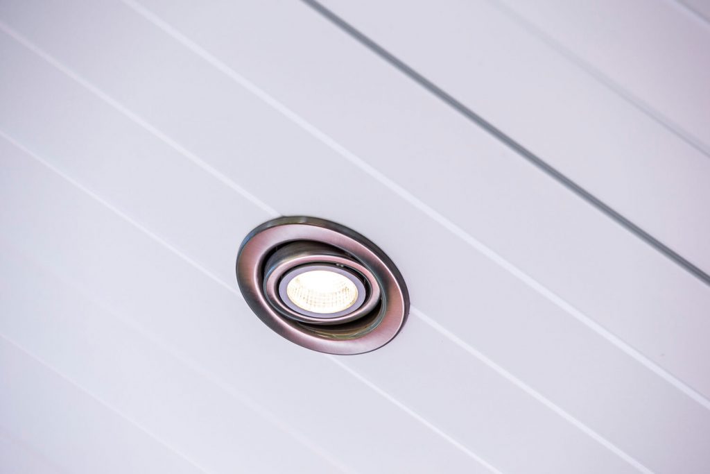 Close-up of an integrated brushed metal gimble LED downlight flush-mounted into a premium white insulated v-groove patio ceiling panel by Emanate and Co.