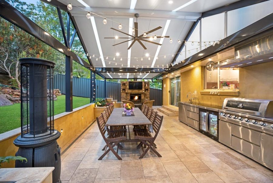 Luxury custom outdoor room and insulated patio roof extension in Berowra, featuring integrated translucent skylight bands, a stainless steel outdoor kitchen, stone paving, and a built-in brick fireplace.