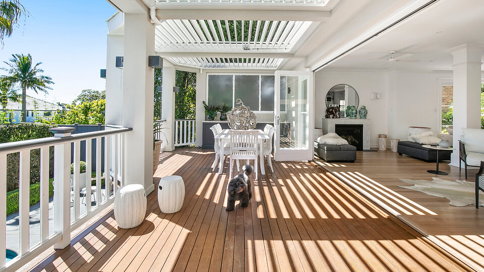 Bright and airy outdoor living space with a louvered roof, white dining furniture, and a seamless connection to the indoor living area, creating an inviting environment for relaxation and entertaining.