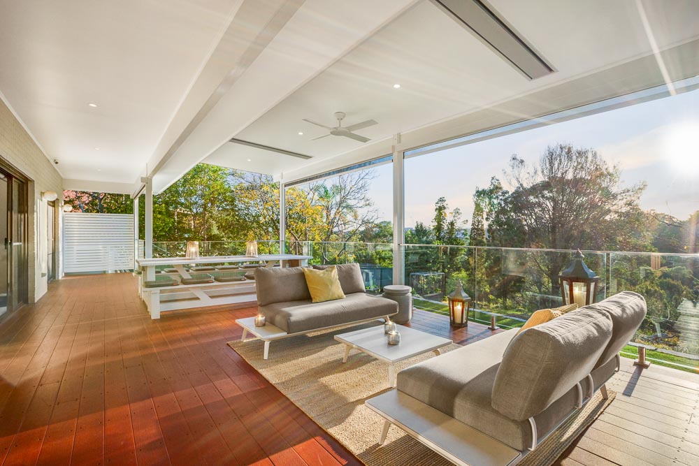 Luxurious outdoor lounge area with modern seating, ambient lighting, and glass balustrades, overlooking a scenic garden, designed for relaxation and enjoying sunset views