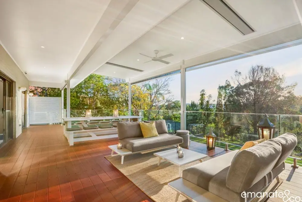 Elevated alfresco living space with glass balustrades, built-in ceiling heaters, and modern furniture for year-round entertaining in leafy Sydney.