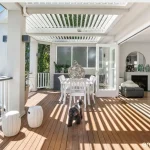 Stylish Northern Beaches patio featuring elevated deck, glass balustrades, and tranquil bushland views for refined outdoor entertaining.