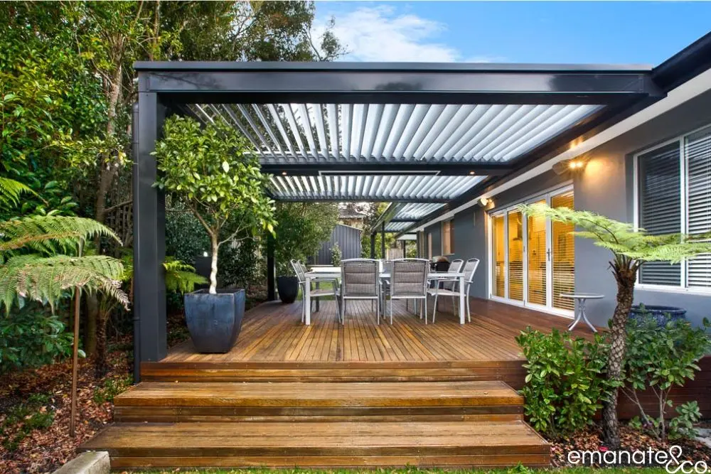 Premium timber deck in Sydney with black-framed louvre patio cover, surrounded by lush garden and elegant alfresco furnishings.