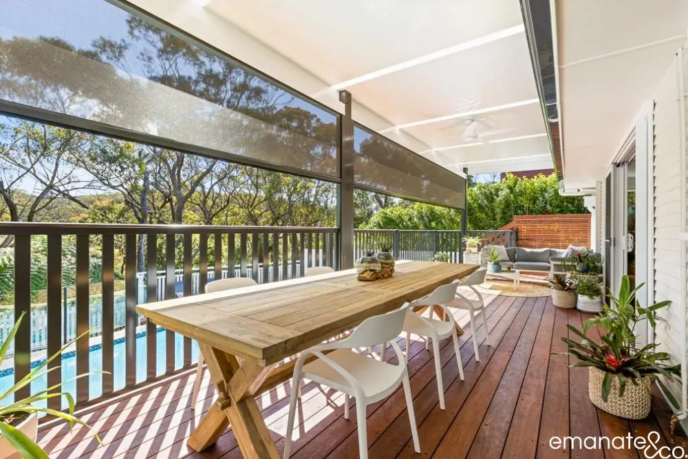 Stylish timber deck with privacy screens, modern dining setup, and greenery in a bushfire zone.