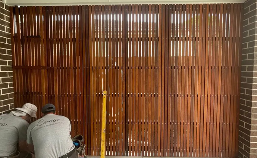 Custom vertical timber batten privacy screen under construction by Emanate and Co builders between residential brick pillars using precision leveling tools.