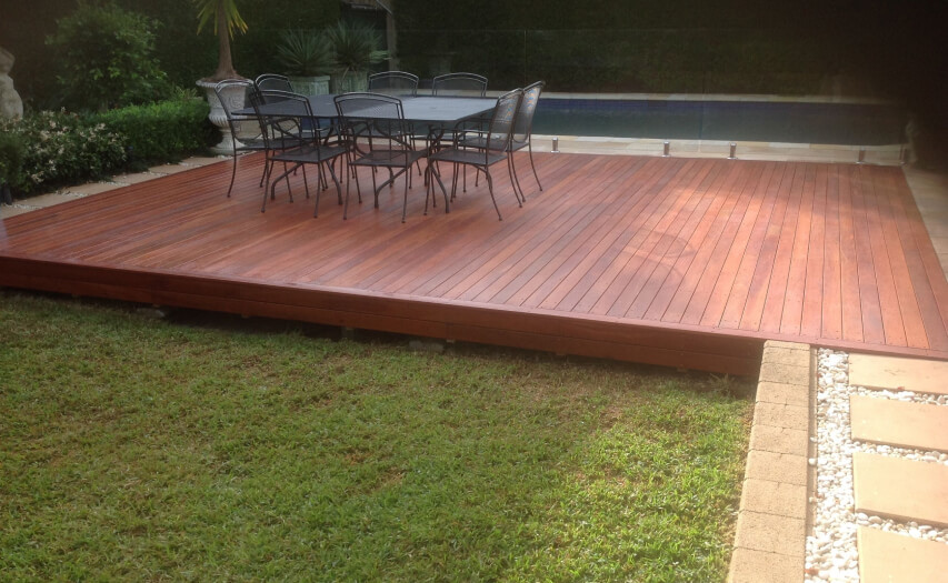 Completed low-to-ground premium hardwood timber deck by Emanate and Co featuring a luxury outdoor dining set installed next to a swimming pool zone.