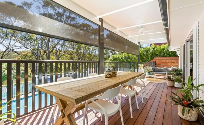 Completed luxury elevated timber deck and integrated patio roof extension by Emanate and Co, featuring automated drop-down privacy screens, vertical safety balustrades, and a premium outdoor dining zone over a swimming pool.