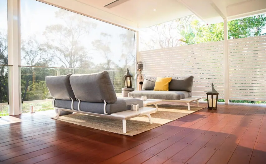 Premium timber deck extension and custom outdoor room by Emanate and Co, featuring modern alfresco lounge furniture, a white horizontal slat privacy screen, glass balustrading, and an insulated patio cover.