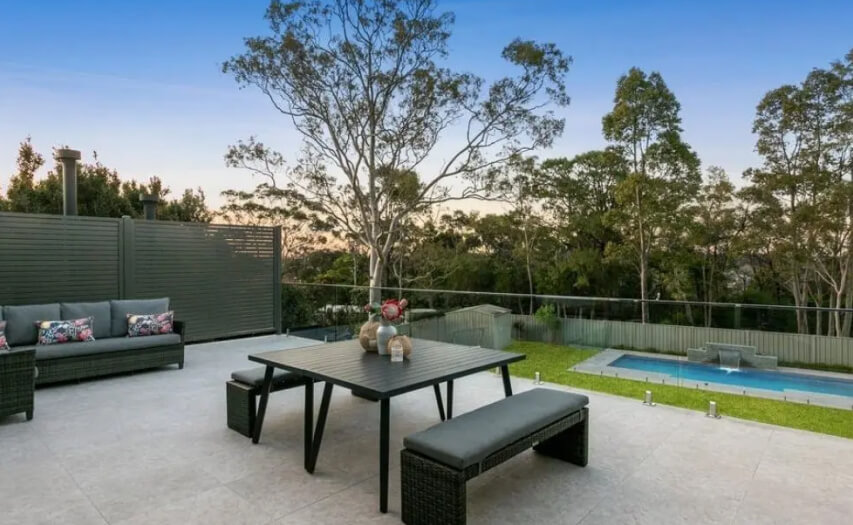 Premium elevated tiled deck extension by Emanate and Co featuring modern stone floor tiles, high-end outdoor furniture staging, a glass balustrade, and integrated privacy screening overlooking a backyard pool.
