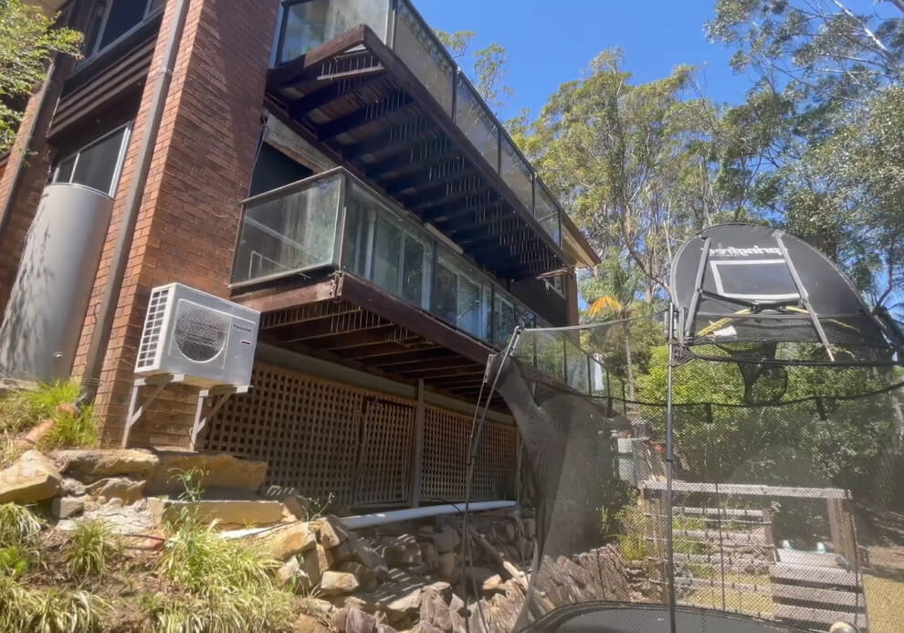 Original multi-level glass panel balconies on a steep sloping block home prior to structural backyard engineering and deck replacement by Emanate and Co.