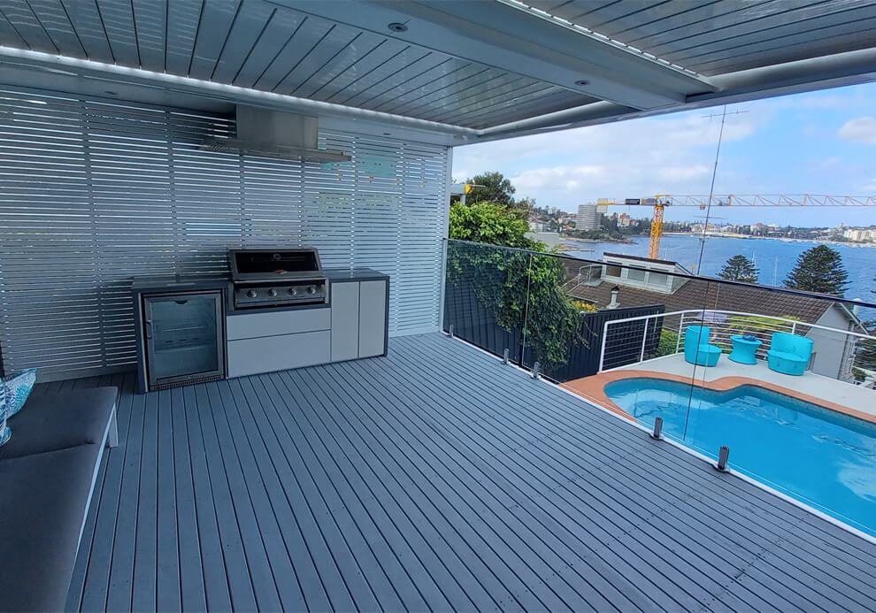 Modern alfresco outdoor kitchen with built-in BBQ, rangehood, beverage fridge, and grey composite deck in Balgowlah Heights by Emanate and Co.