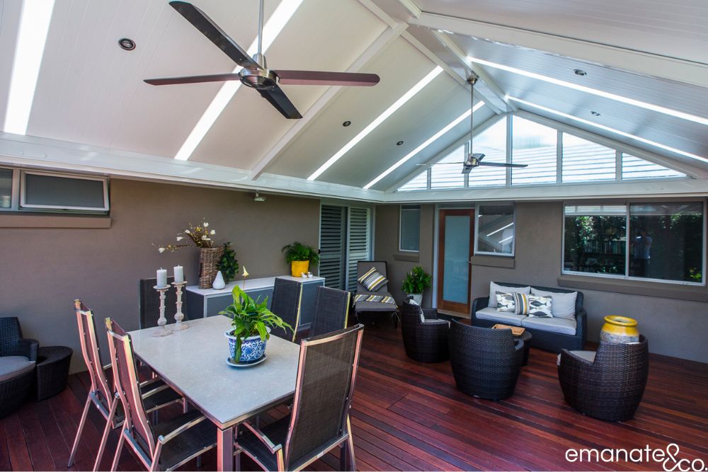 Large hardwood outdoor room with dining and lounge zones beneath a gabled insulated patio cover featuring skylights, fans and recessed lighting.