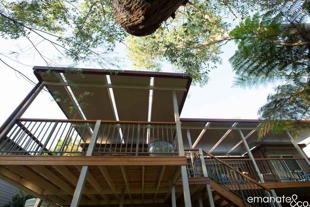 Low-angle view of an elevated timber deck and insulated patio cover designed around a sloping, tree-filled Sydney backyard.