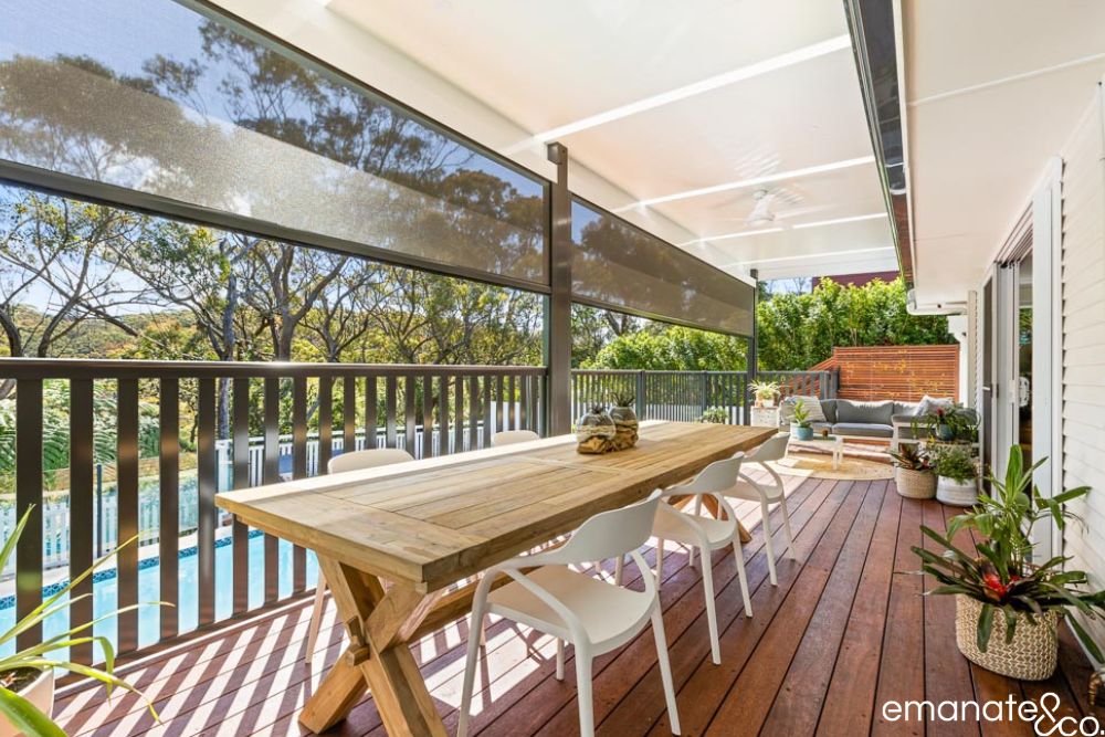 Poolside timber deck beneath an insulated patio cover, with retractable sun screens, alfresco dining and lounge areas at a Sydney home.