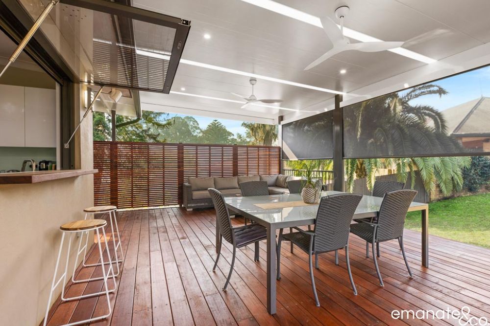 Spacious timber deck and alfresco dining area beneath an insulated patio roof, with ceiling fans, privacy screens and an outdoor servery.