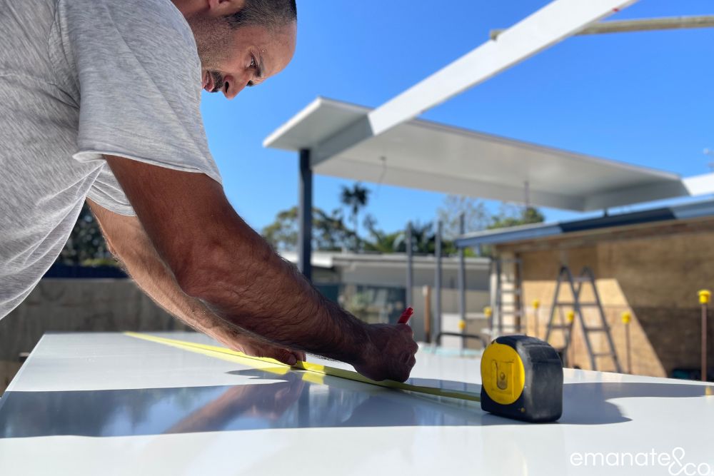 Emanate & Co. builder measuring insulated roof panels during construction of a custom patio cover beside a Sydney swimming pool.