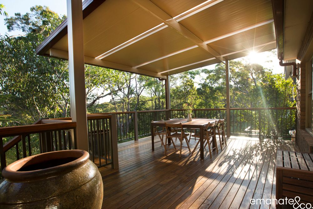 Elevated timber deck with an insulated patio cover creates a sheltered outdoor dining space overlooking the leafy bushland surrounding a Sydney home.