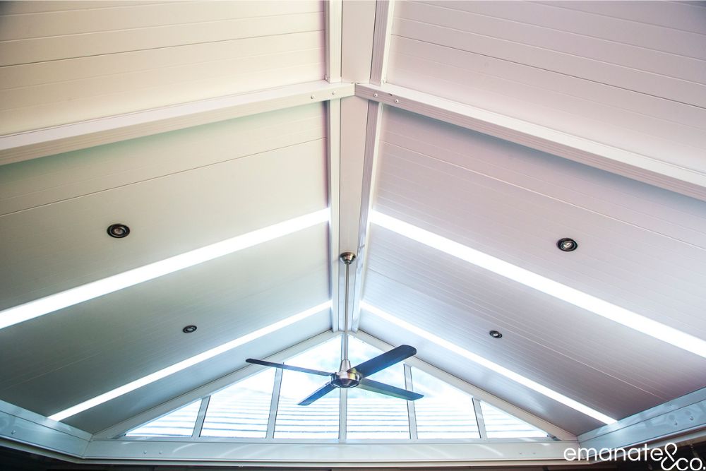 Close-up of a gabled insulated patio ceiling with skylight strips, recessed lighting, ceiling fan and glazed triangular end panels.