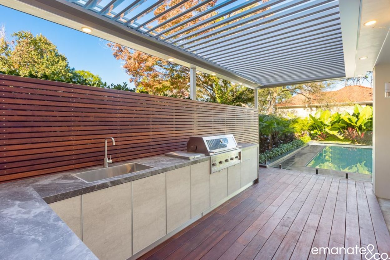 Wahroonga outdoor kitchen with stone benchtops, built-in barbecue, hardwood deck and opening louvred roof overlooking the swimming pool.