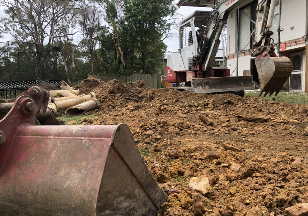 Excavator preparing ground and pipe infrastructure for deck construction over an easement by Emanate and Co.