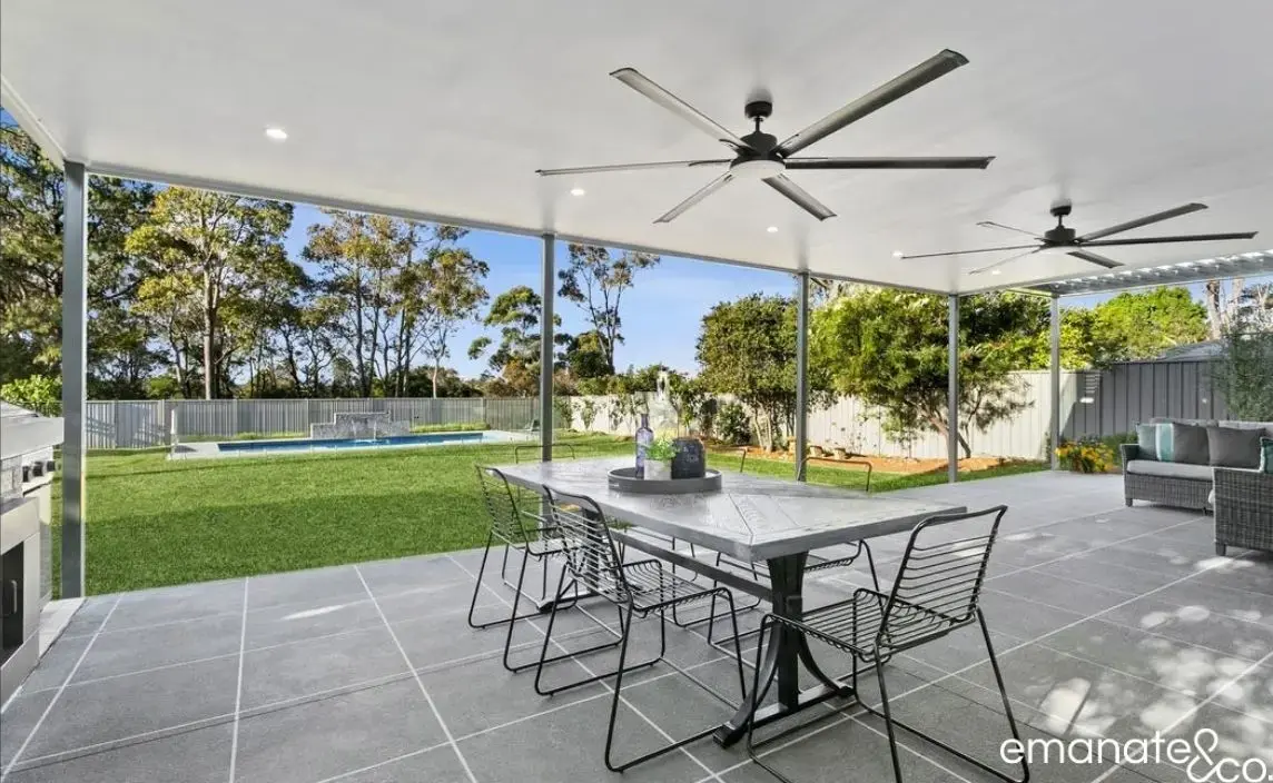 A covered outdoor dining space with tiled flooring, ceiling fans, and a poolside view, offering a functional and stylish outdoor alfresco experience.