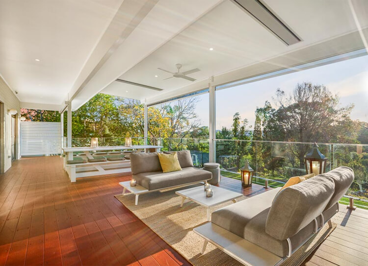 Custom flyover patio extension with lined ceiling, integrated heaters, glass balustrade, and composite deck in West Pymble by Emanate and Co.