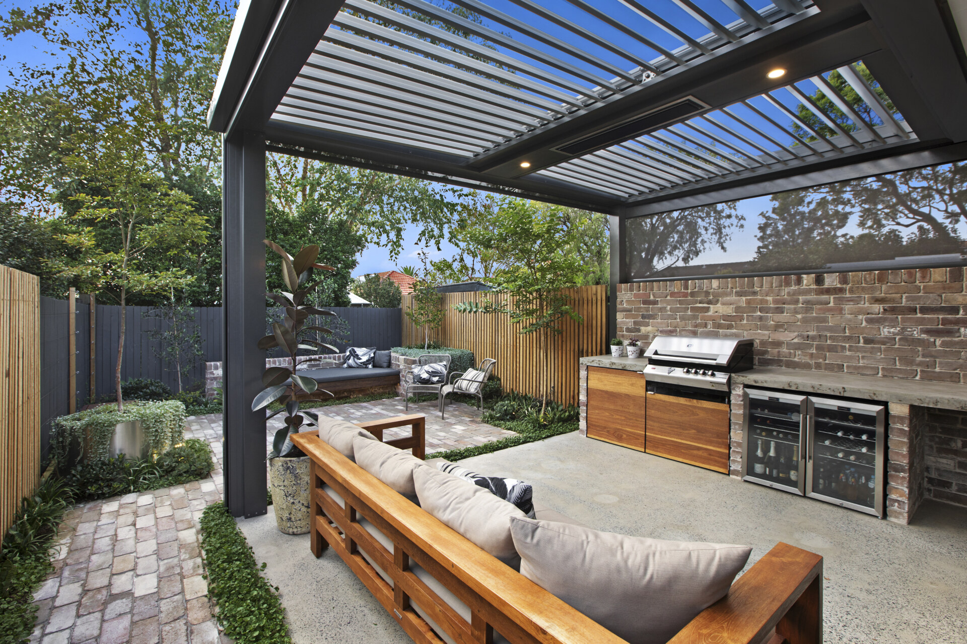 A modern outdoor entertaining space with a built-in barbecue, drinks fridge, and custom opening roof